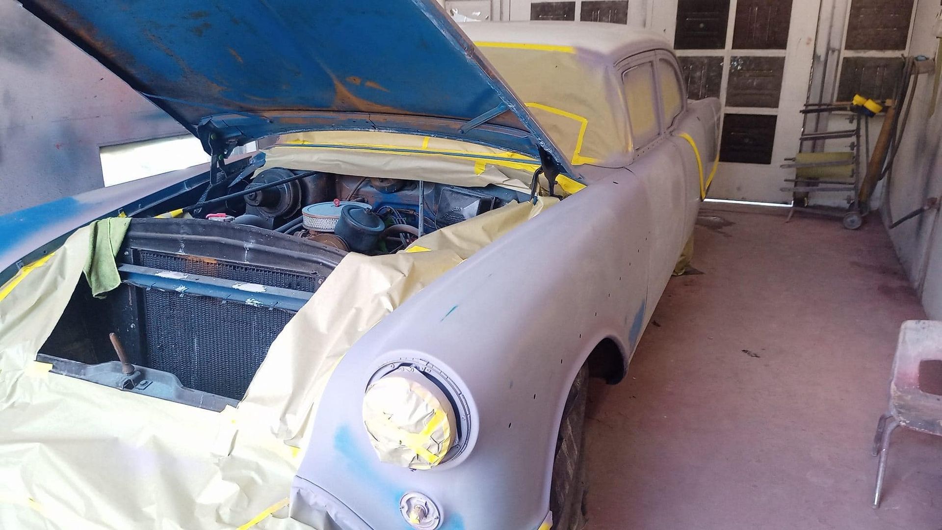 Classic car in primer, masked and prepped for paint in a garage.