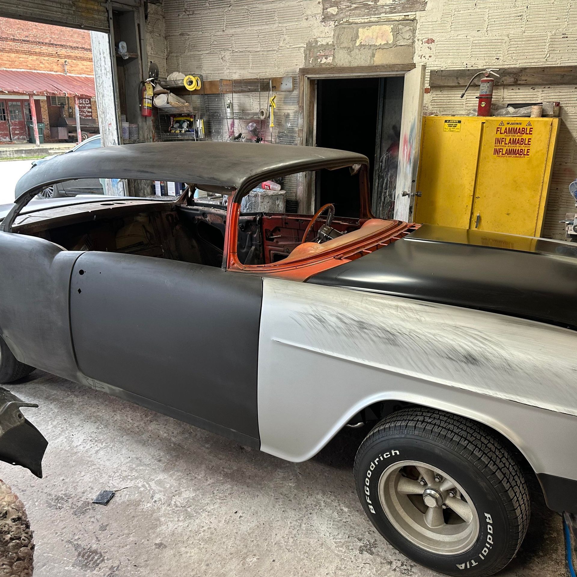 Classic car in a garage under restoration. Body panels are various colors: black, gray, and orange.