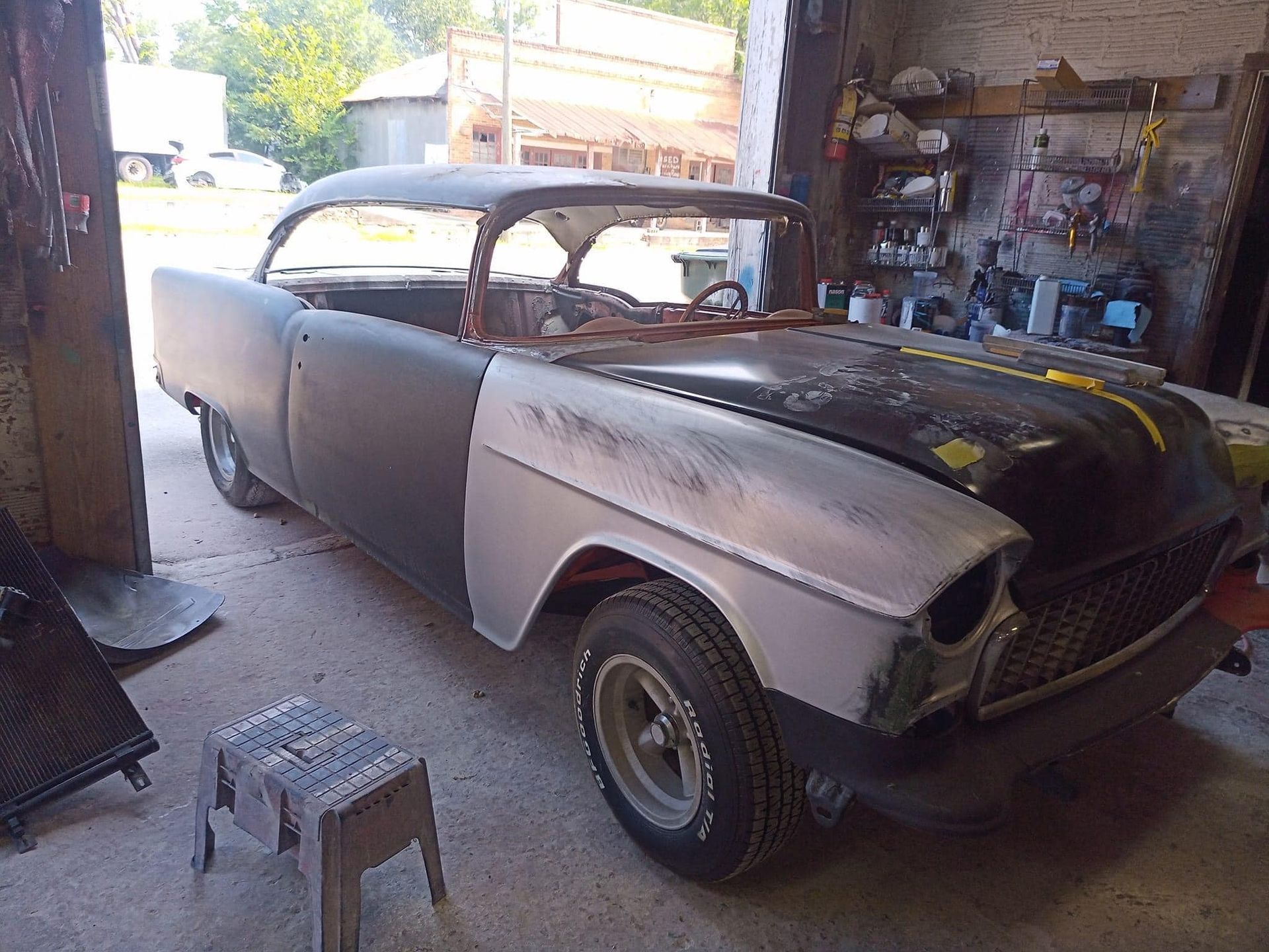 Classic car body being restored in a garage; gray, black, and rust colors prominent.