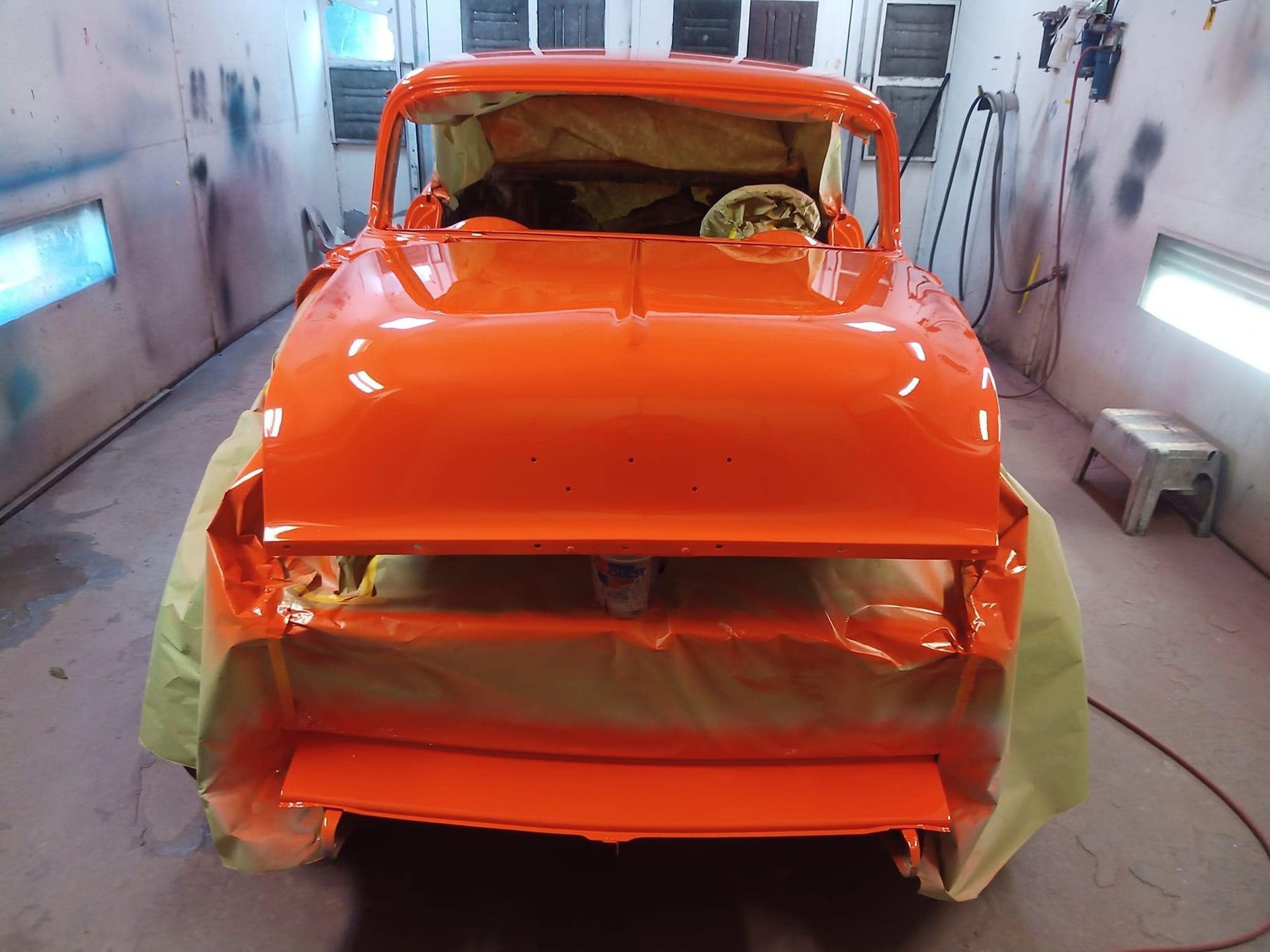 Orange classic truck in a spray paint booth, undergoing restoration.