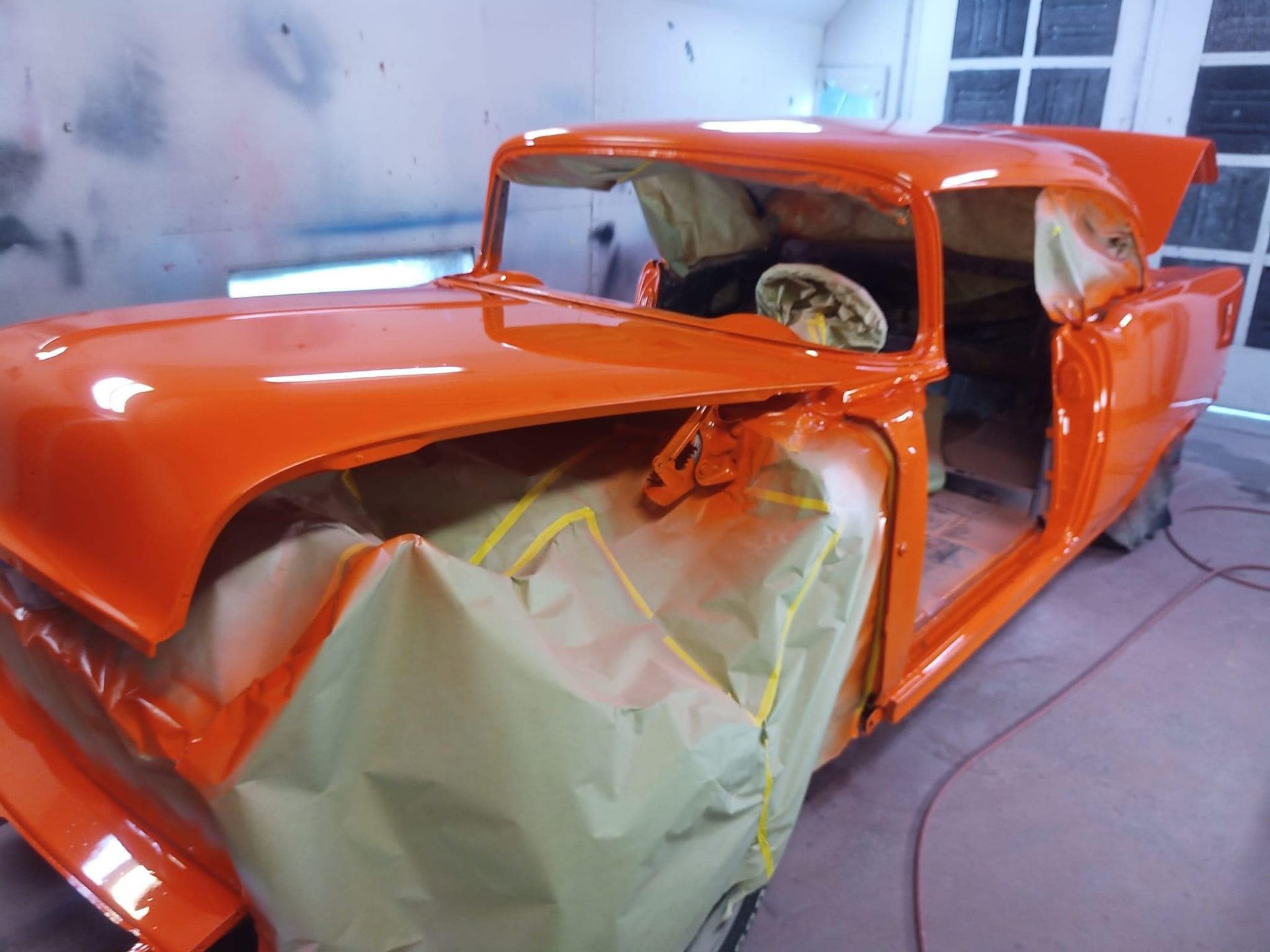Classic orange car, partially masked, in a spray painting booth.