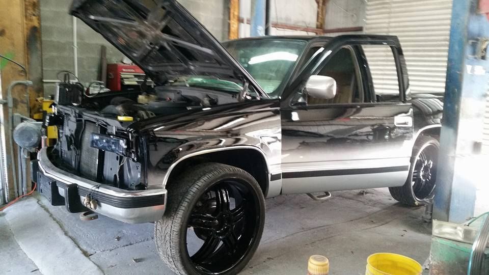 Black and silver pickup truck with open hood in a garage.