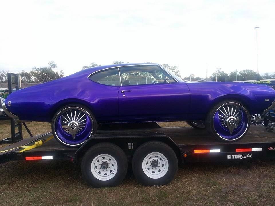 Purple classic car on a trailer with oversized chrome rims.