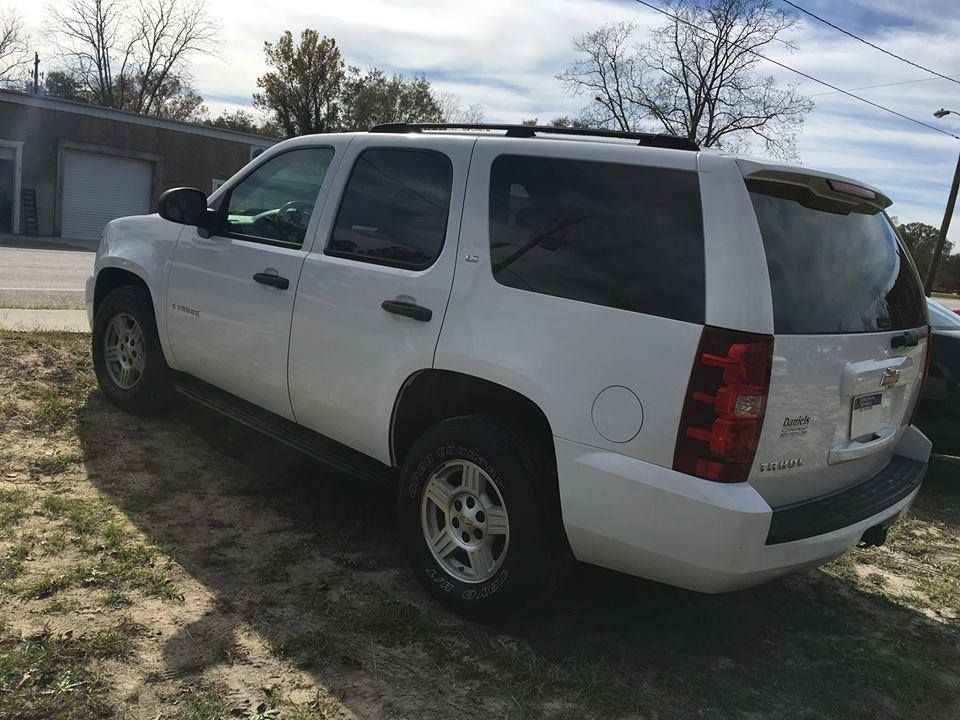 White Chevrolet Tahoe SUV parked on grass next to a road, sunny day.