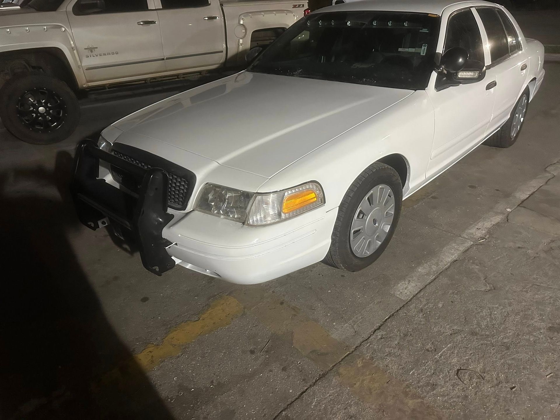 White Crown Victoria police car parked outside at night.