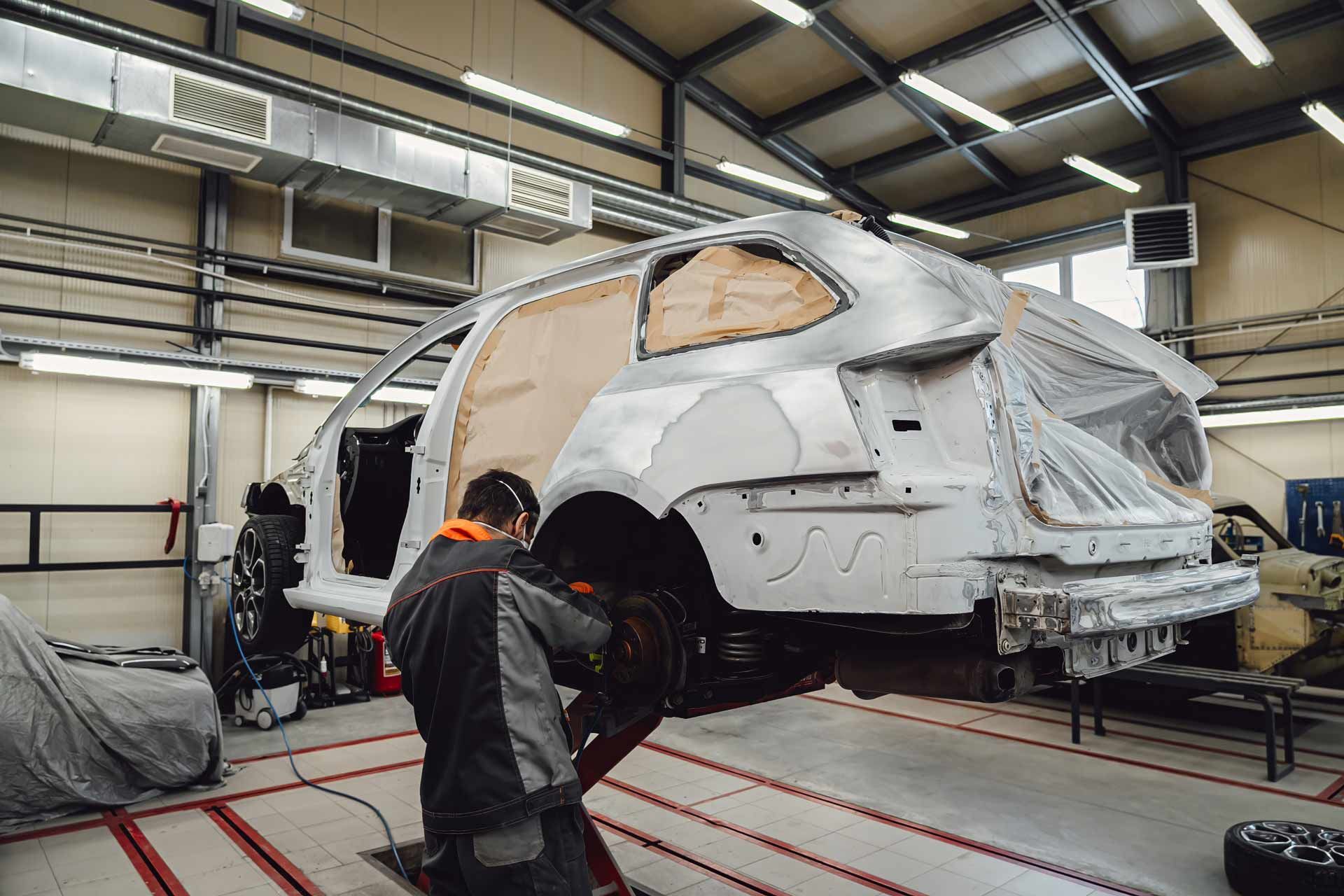 Mechanic working on a car in a body shop. The car is on a lift, partially disassembled and primed.