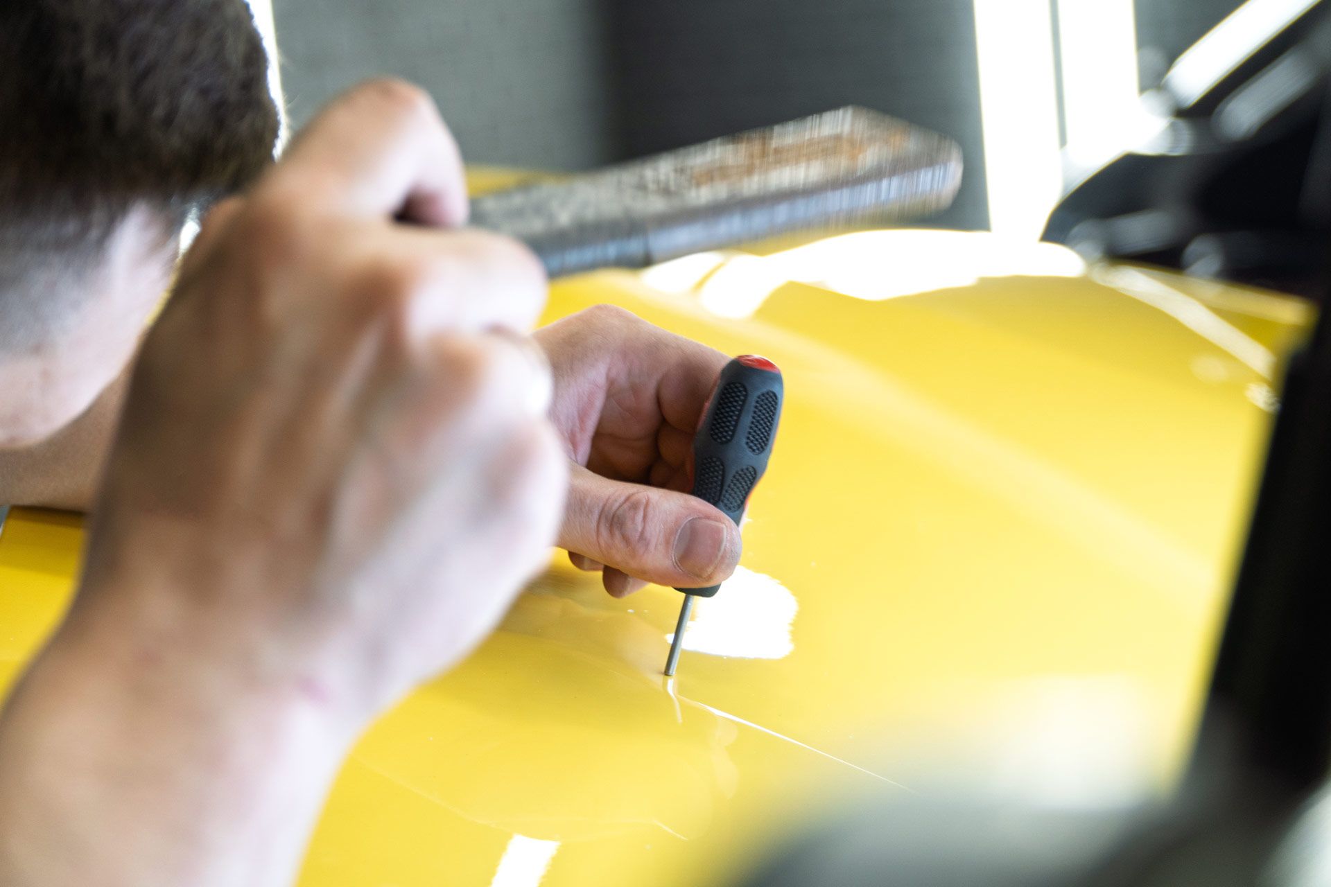 Person using a tool to repair a scratch on a yellow car's surface.