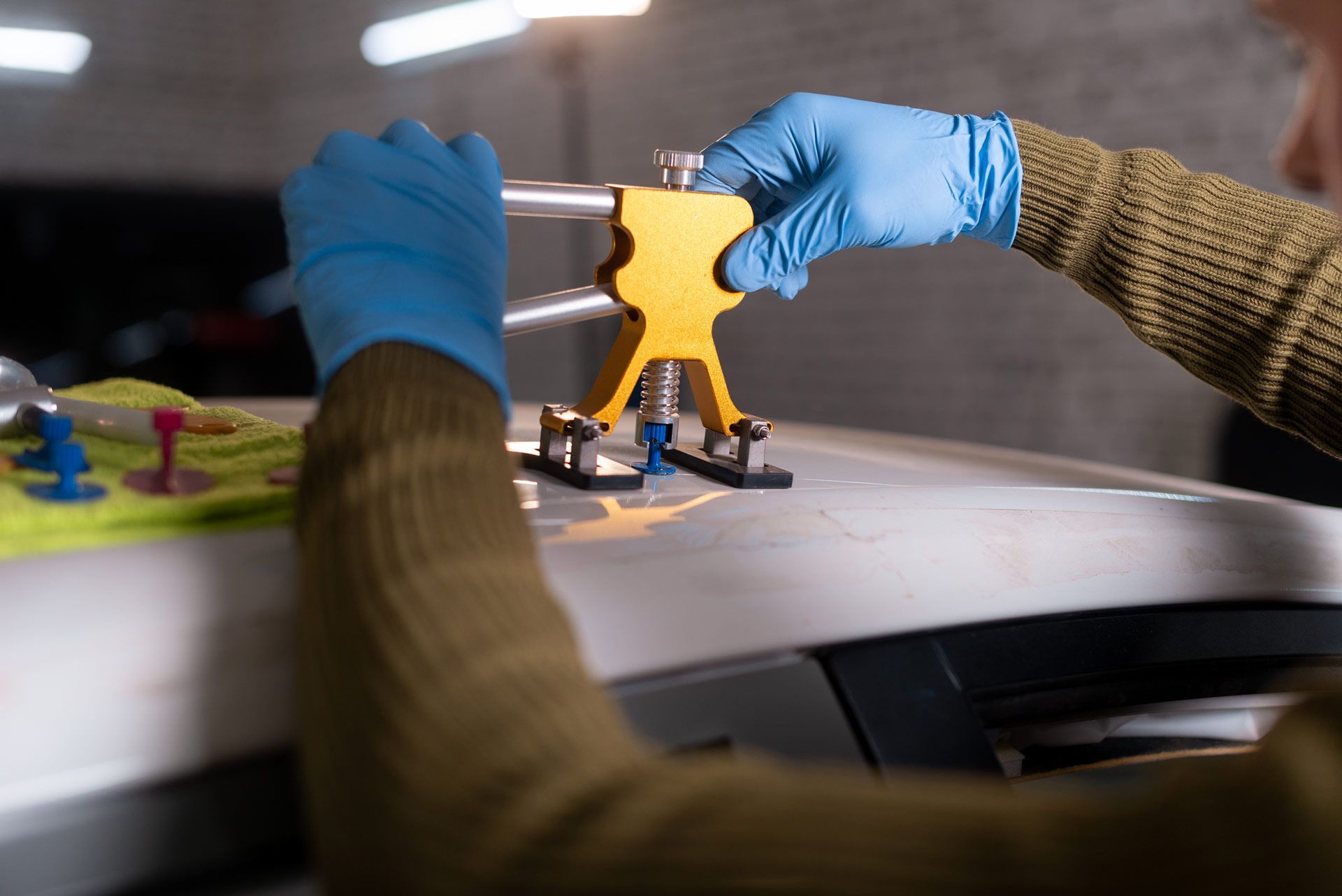 Person in blue gloves using dent repair tool on a white car roof.