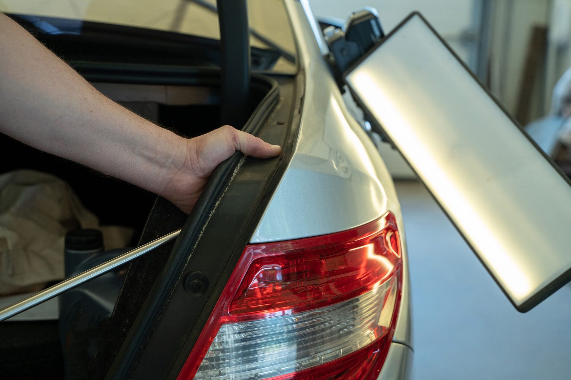Person using a dent repair tool on a silver car's trunk. The tool reflects light.