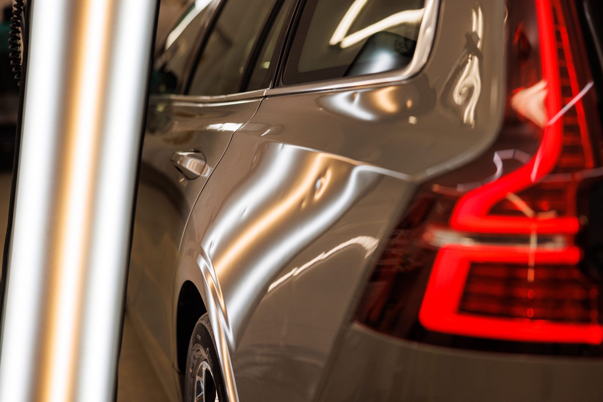 Silver car body with dent, being inspected under bright lights.