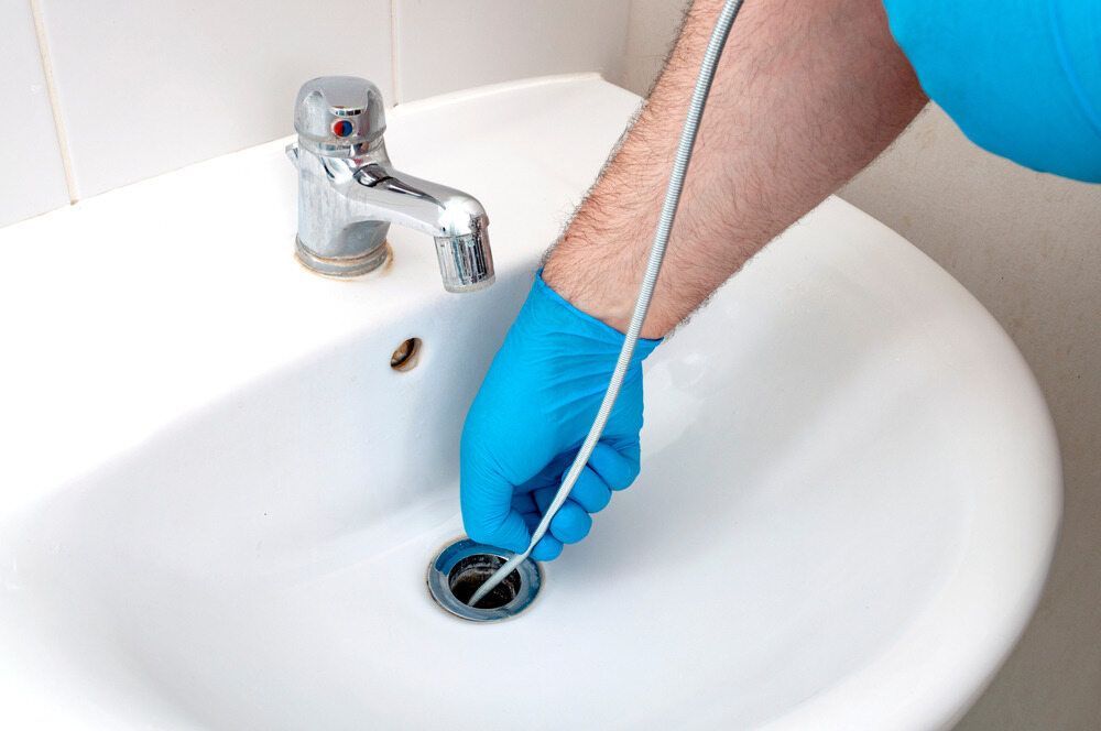 A Person Is Cleaning A Sink With A Hose — C.J Honeysett Plumbing In Narromine, NSW