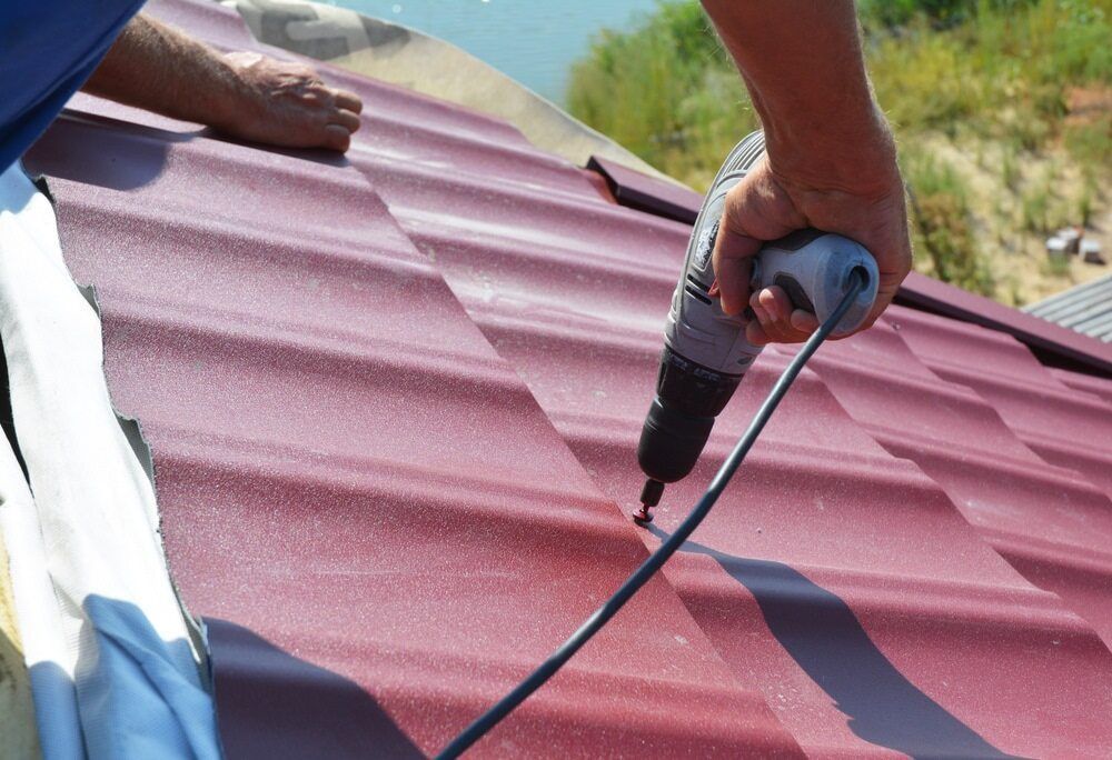 A Man Is Using A Drill On A Red Roof — C.J Honeysett Plumbing In Dubbo, NSW