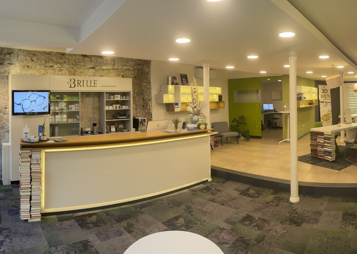 Empfangstresen in einem Büro; weißer Tresen, Ziegelwand, Wartebereich mit Computer.