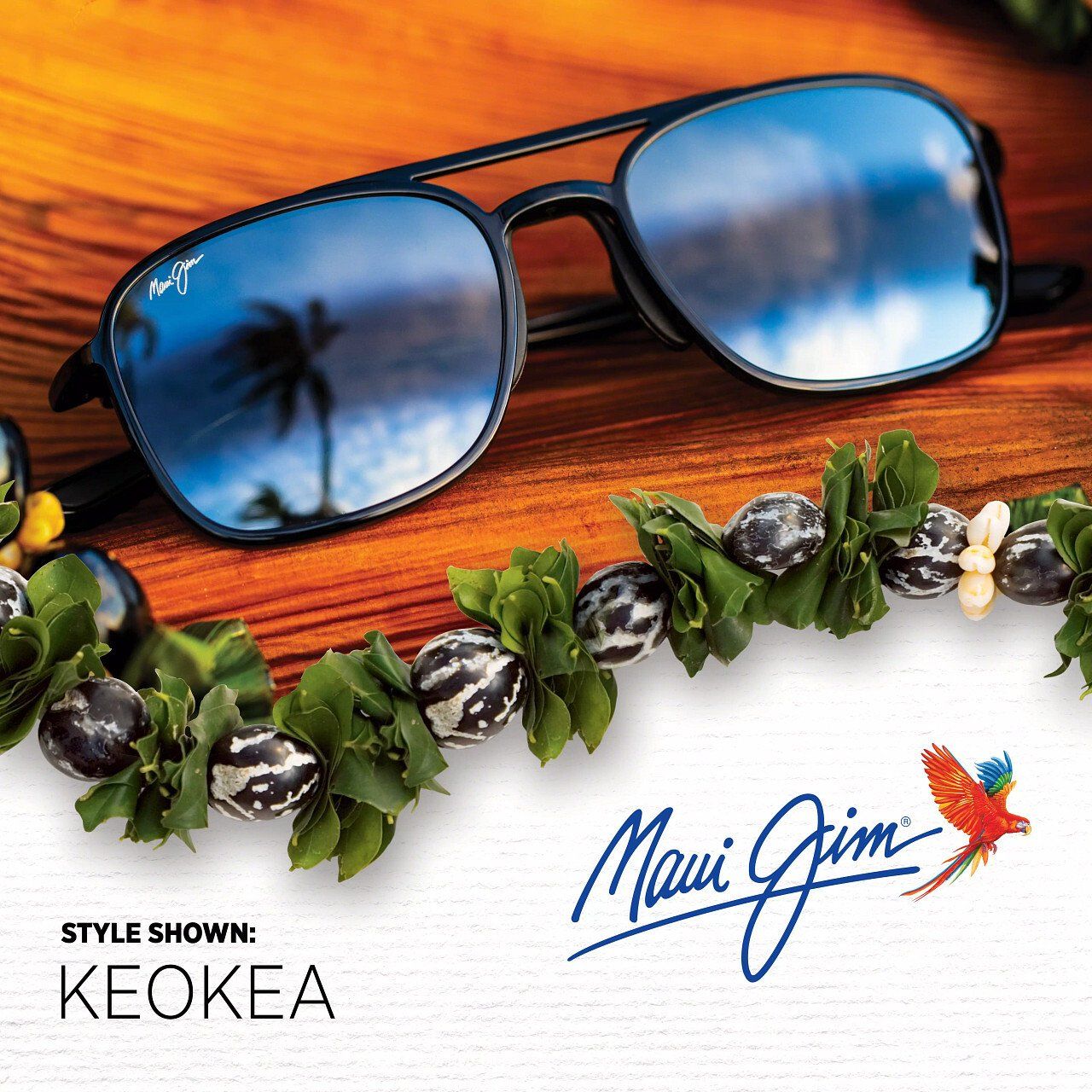 Maui Jim-Sonnenbrille (Keokea-Stil) auf Holz mit einer Blumenkette; Spiegelungen von Himmel/Palme.