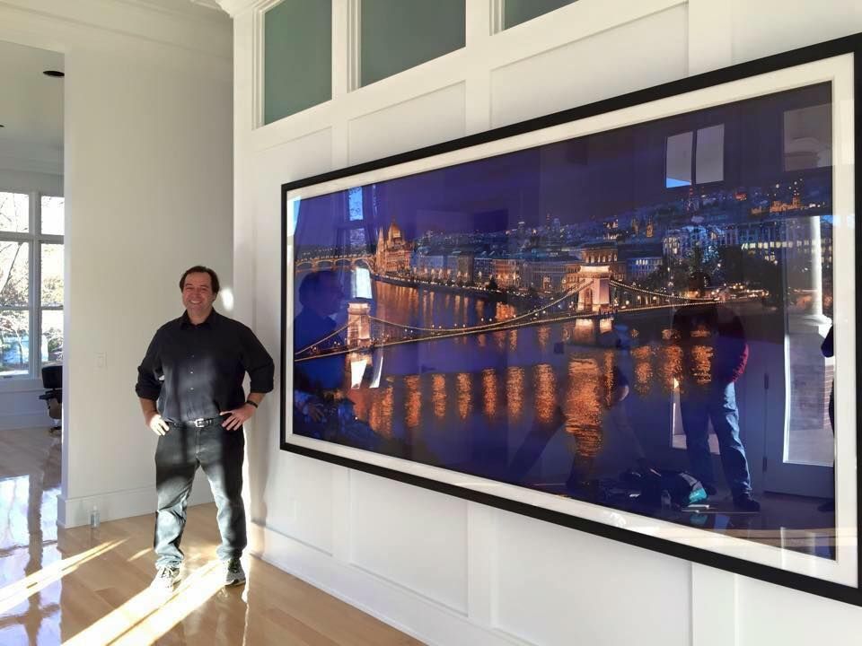 Watercolor Artist Paul Jackson Standing Next to a Painting of a City at Night.