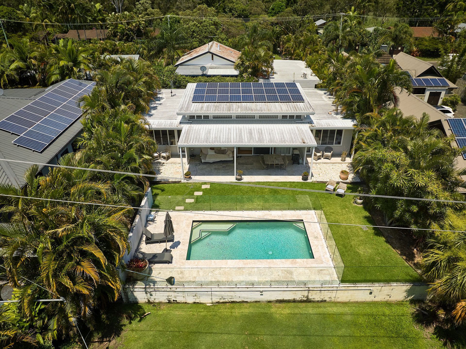 An aerial view of a house with a swimming pool and solar panels on the roof.