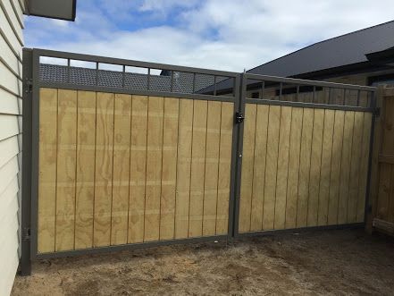 A gray fence is in front of a house with a slate roof.