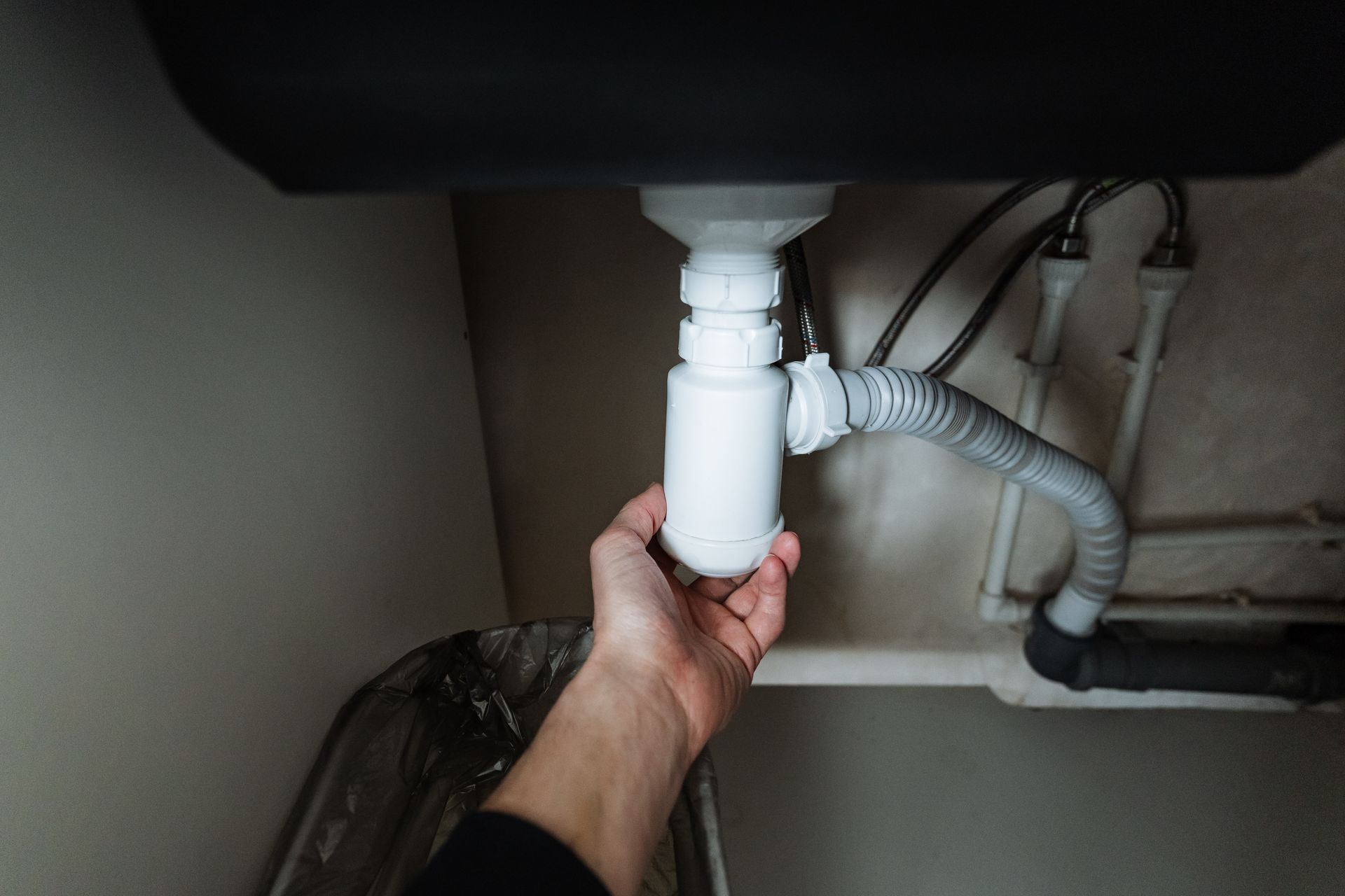 A person's hand is reaching for the plumbing under a sink, likely to repair it.