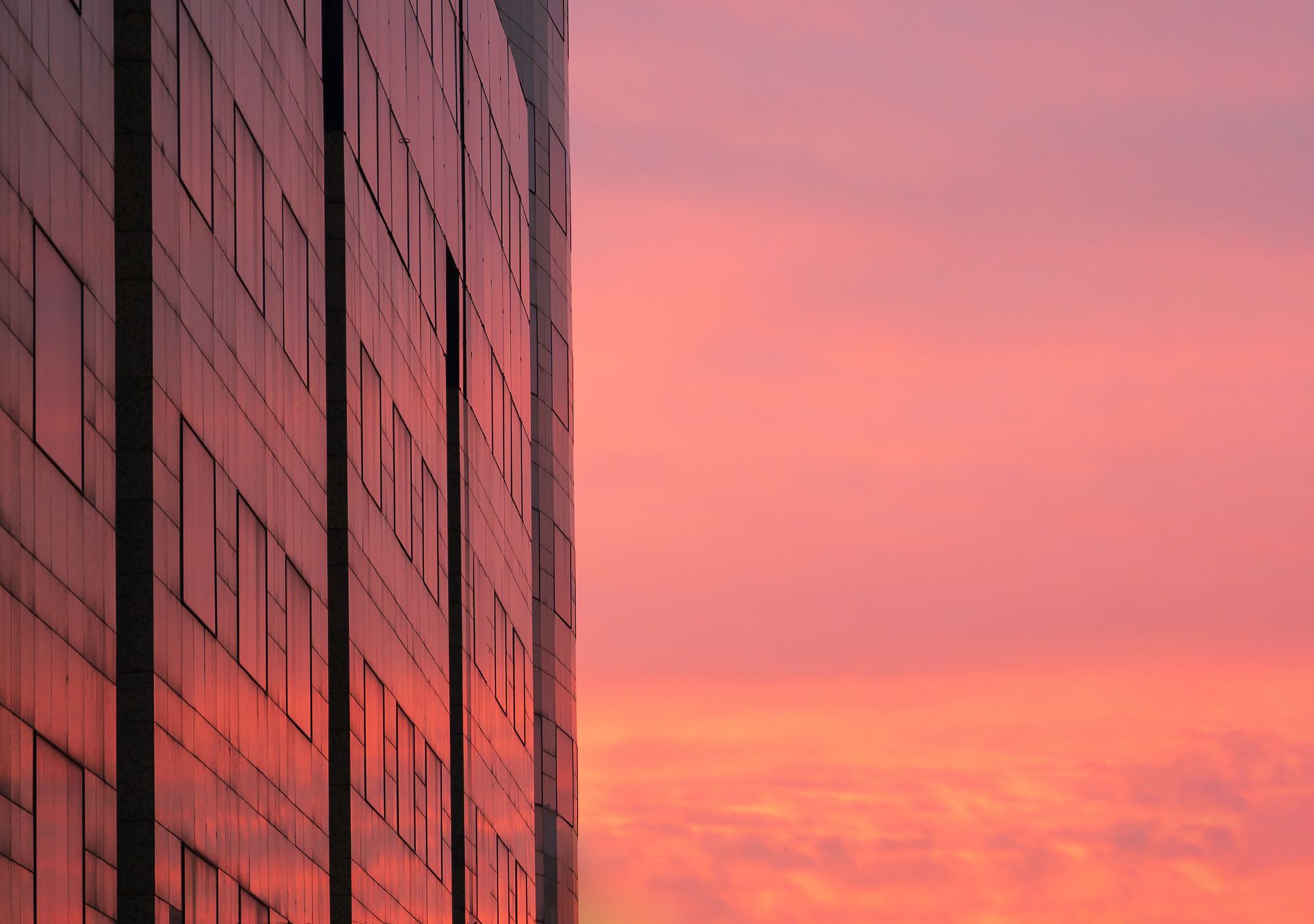 Glass building facade reflecting a pink-orange sunset sky