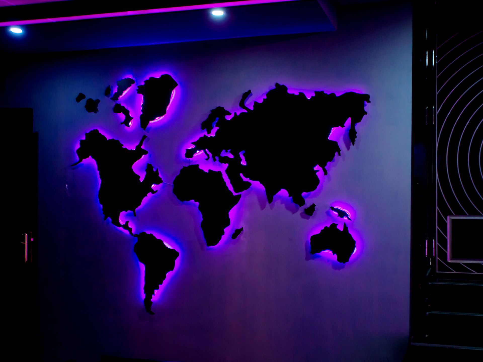 Backlit world map wall art glowing purple in a dark room