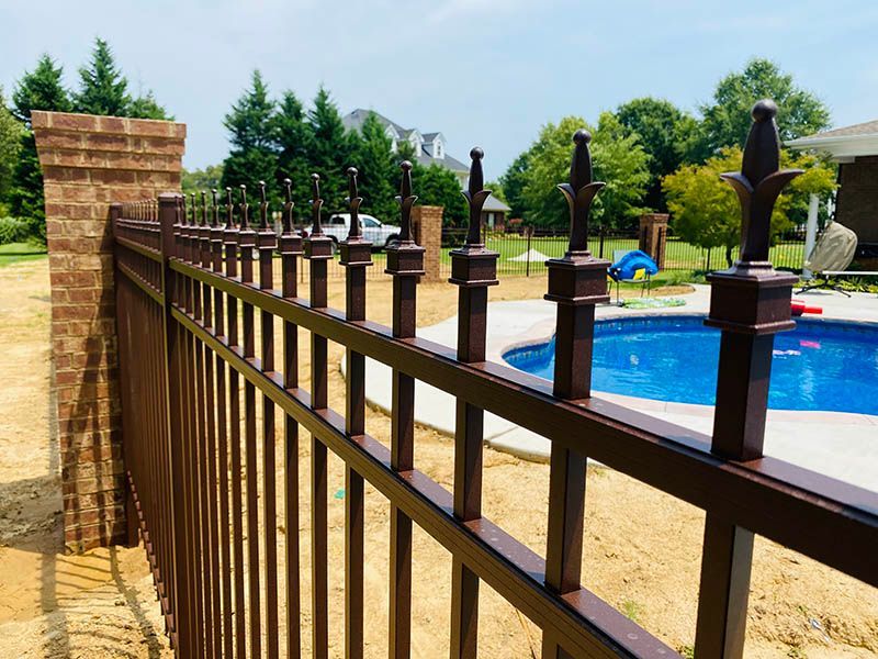 Brown metal fence with decorative finials around a pool in a yard.