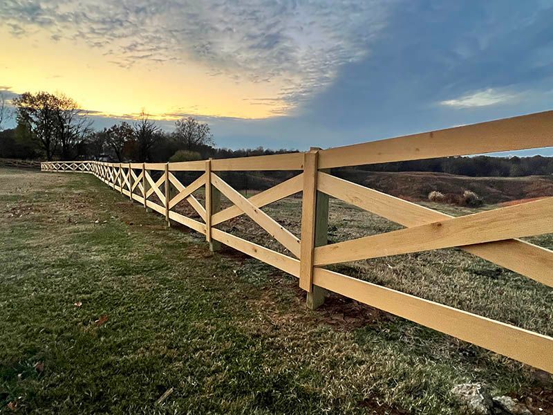 Wooden fence with X-shaped bracing in a grassy field, under a cloudy sky at sunset.