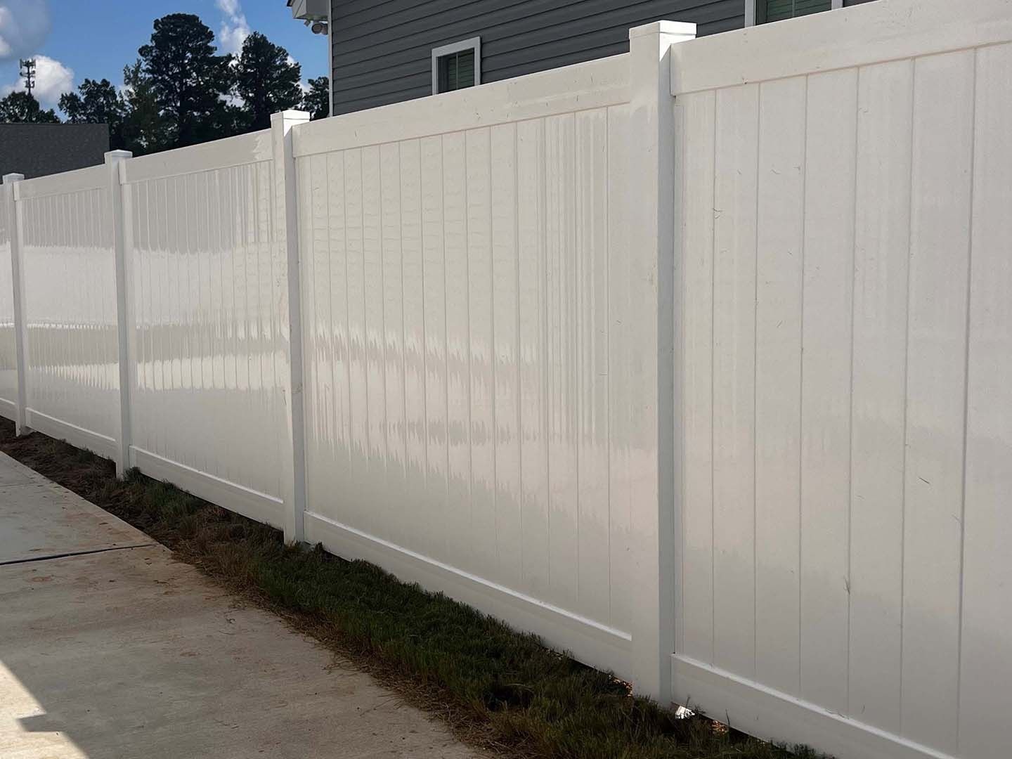 White vinyl privacy fence alongside a concrete walkway and grassy area.