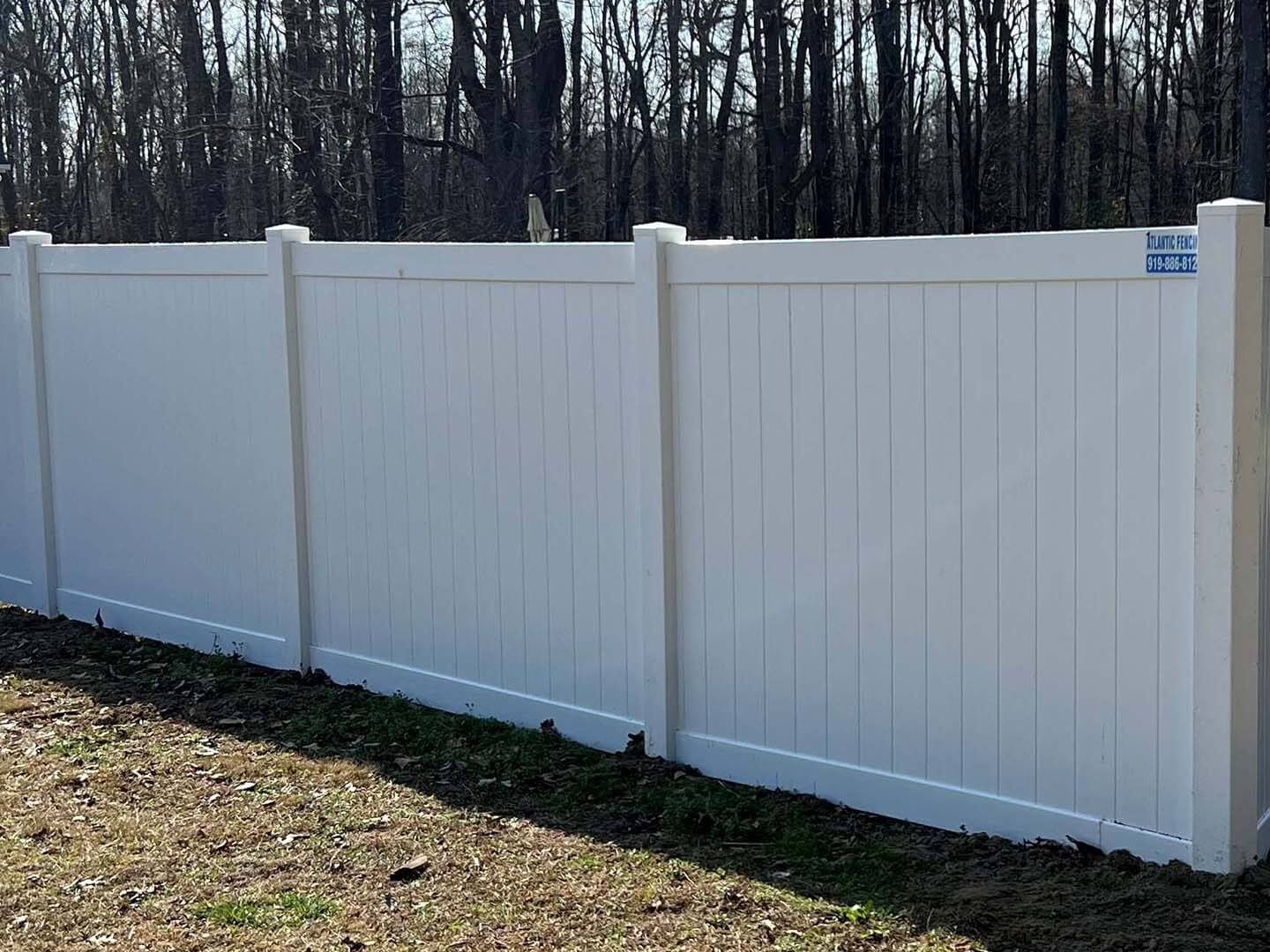 White vinyl fence in a yard with trees in the background.