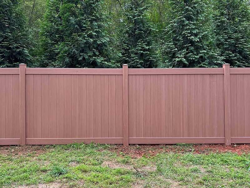 Brown privacy fence in a yard with green grass, with evergreen trees in the background.
