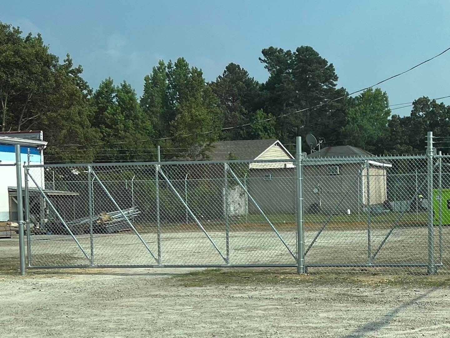 Chain-link fence in front of a building and trees under a cloudy sky.