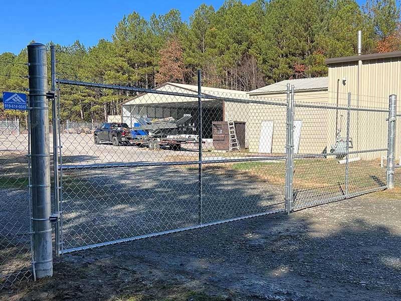 Chain-link fence with open gate; building and parked vehicles in the background.