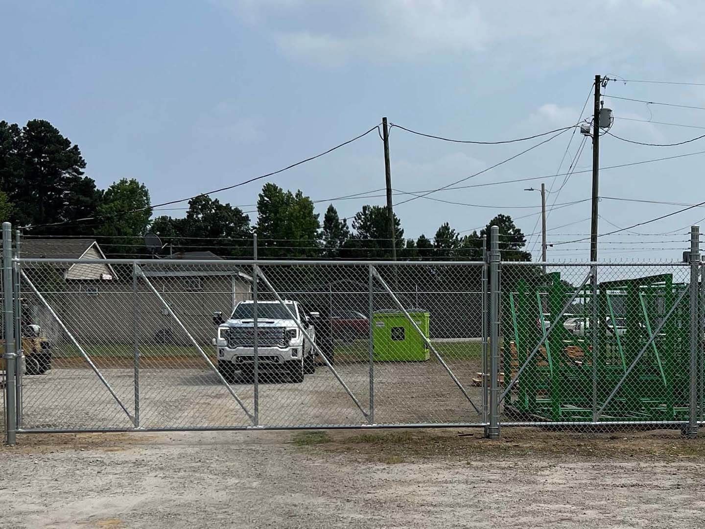 Chain link fence, gate, truck parked inside. Green box and utility poles in the background.