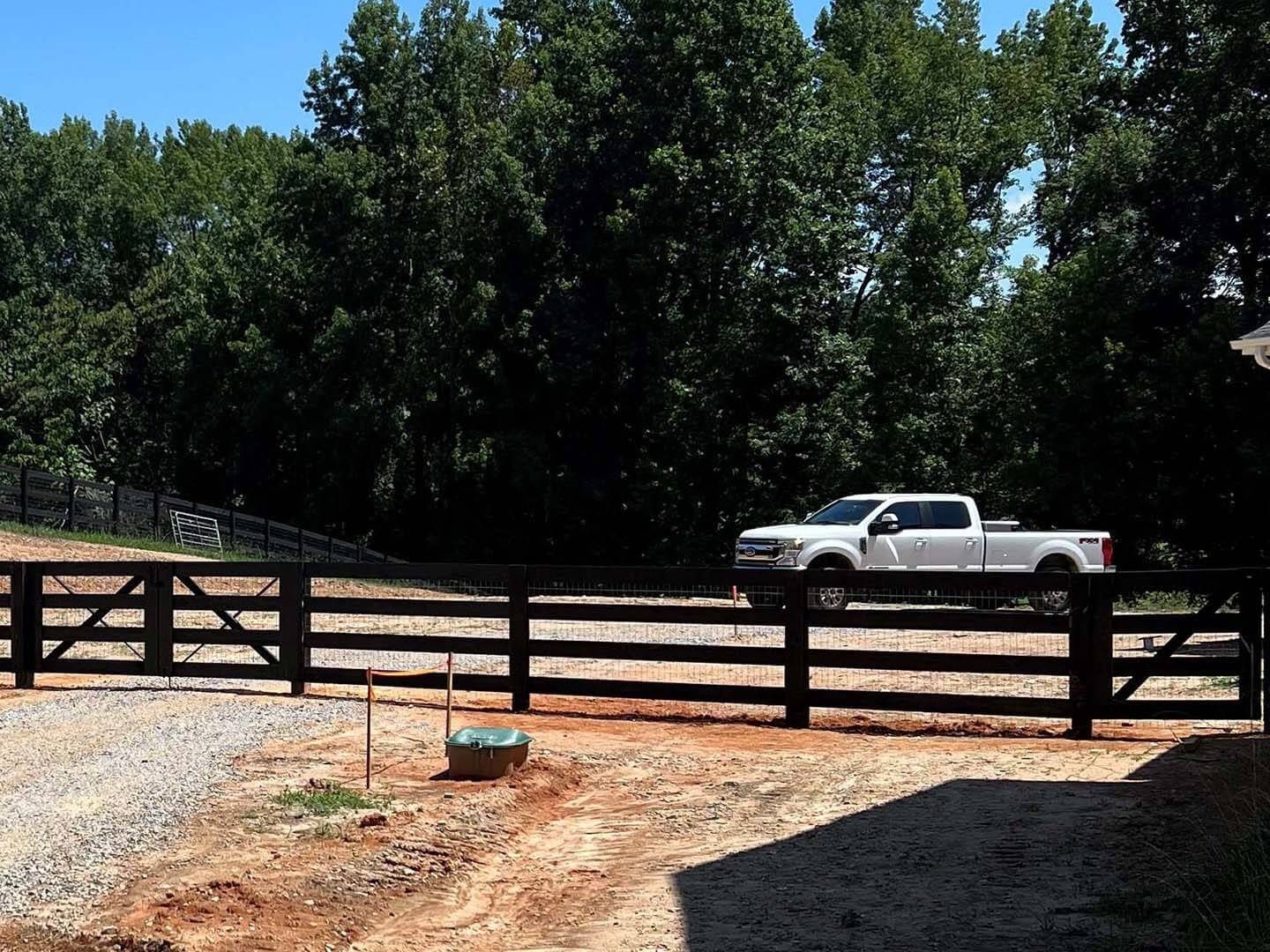 White truck parked behind a dark wood fence. Gravel driveway with trees in the background.