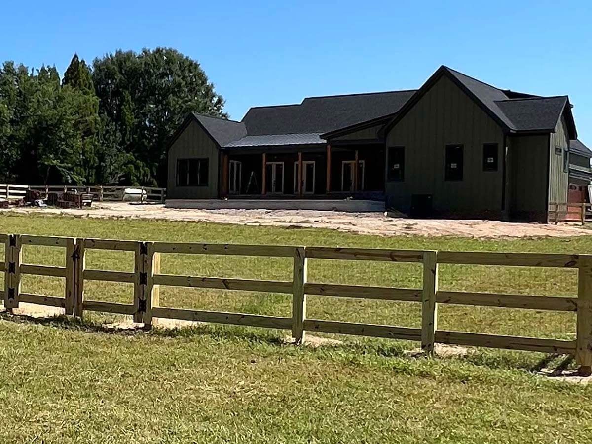 Green house with wooden fence in front, blue sky.