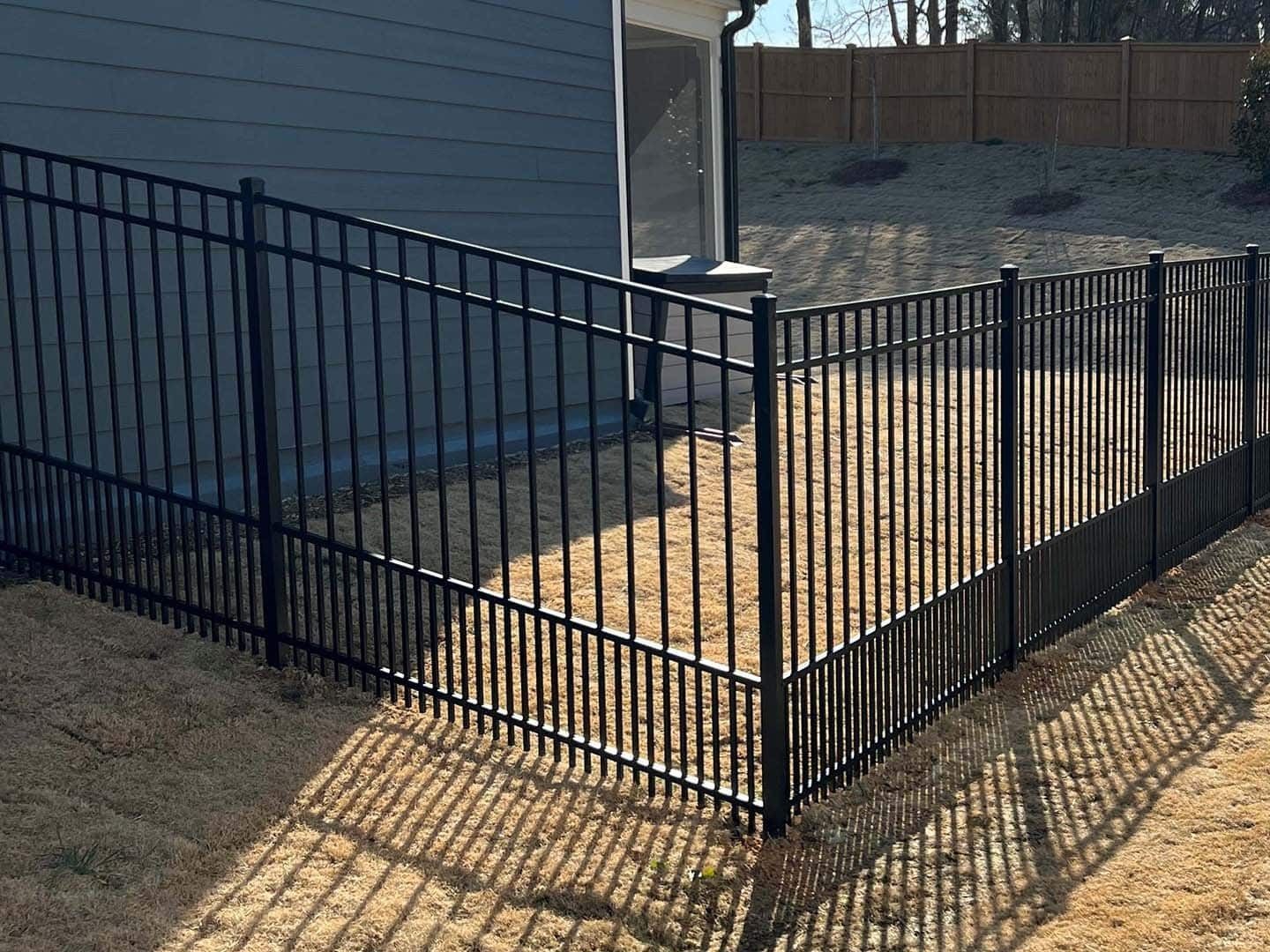 Black metal fence in yard, bordering a house and sunny backyard.