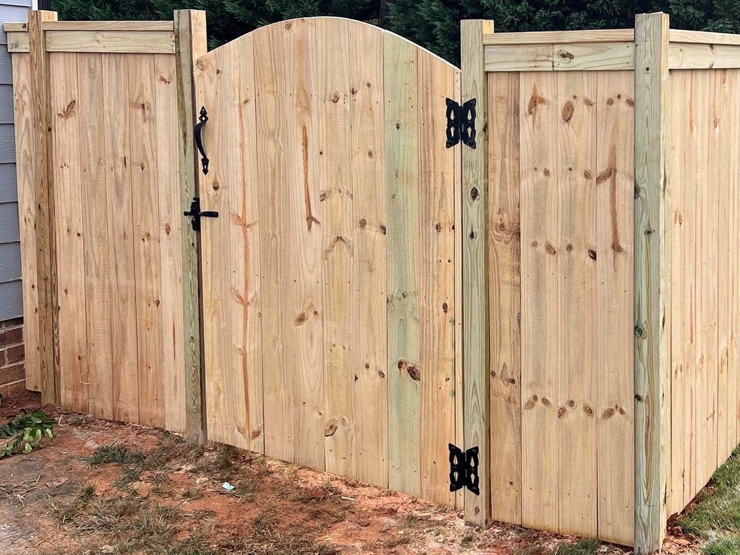 Wooden fence with arched gate; the fence is unfinished light brown with black hardware.