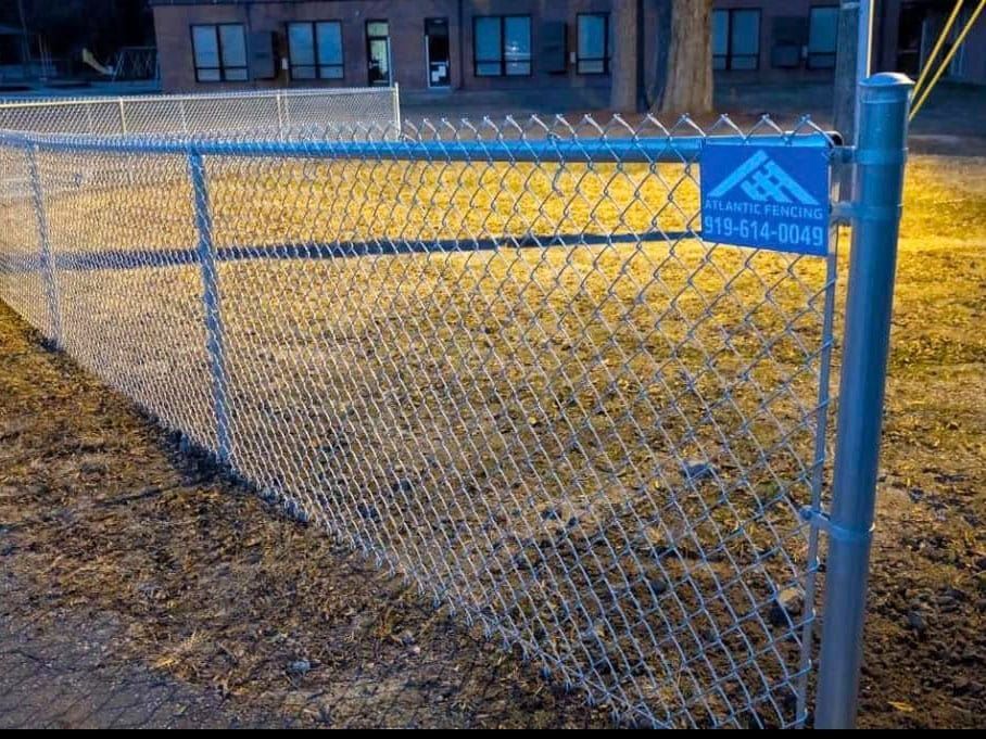 Chain-link fence with a blue sign, set in a yard at dusk.