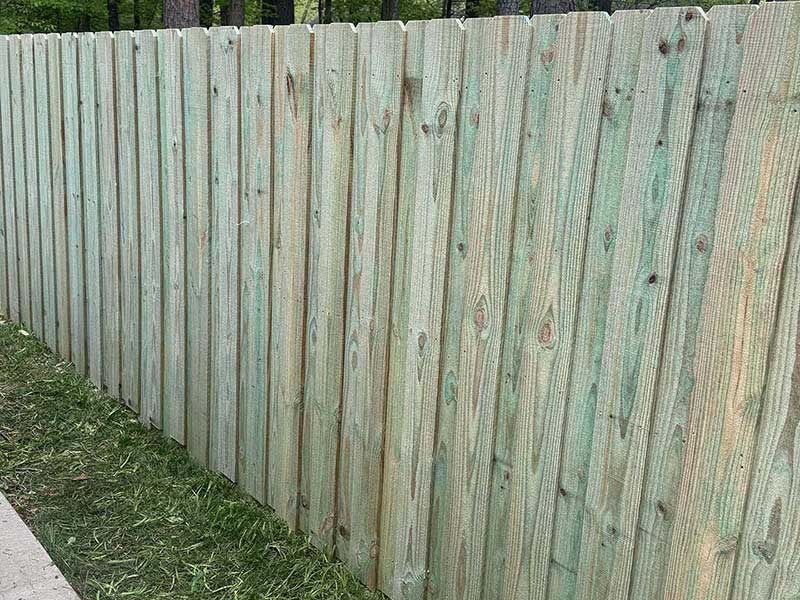 Green-toned wooden fence with vertical planks, standing along a grassy edge, under sunlight.