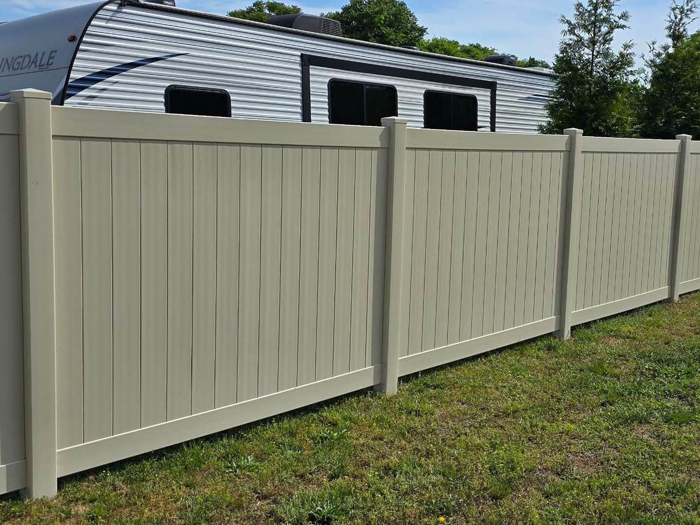 Tan vinyl fence in front of a camper on green grass.