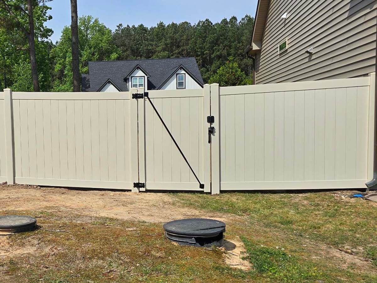 Beige vinyl fence with gate in a yard, house in the background.