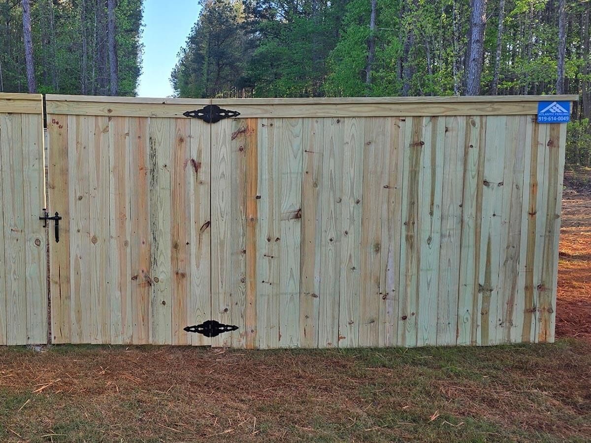 Wooden privacy fence with gate, set in a grassy area, with a treeline in the background.