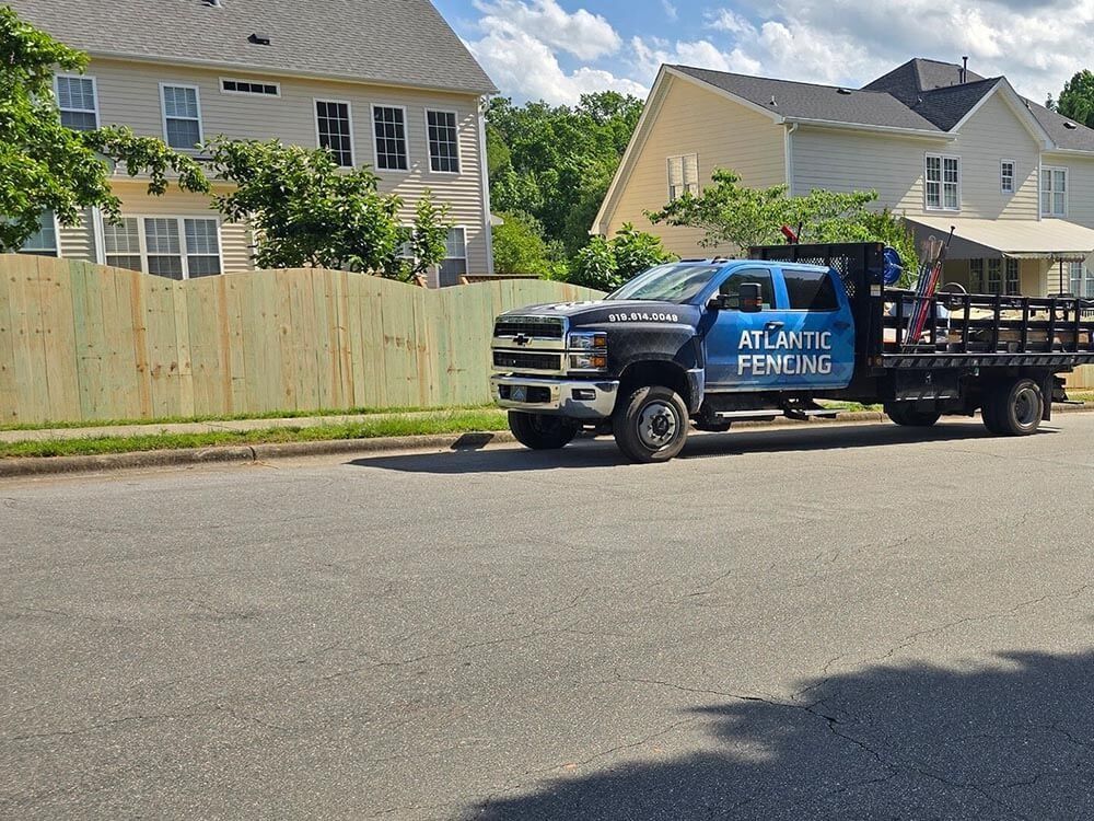 A blue Atlantic Fencing truck parked on a street next to a newly built wooden fence. Houses in the background.