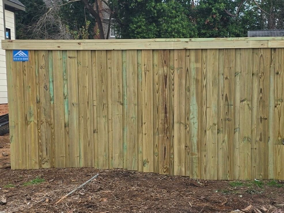 Wooden fence with vertical planks, light green-brown. Blue sign visible on the fence. Outdoors.