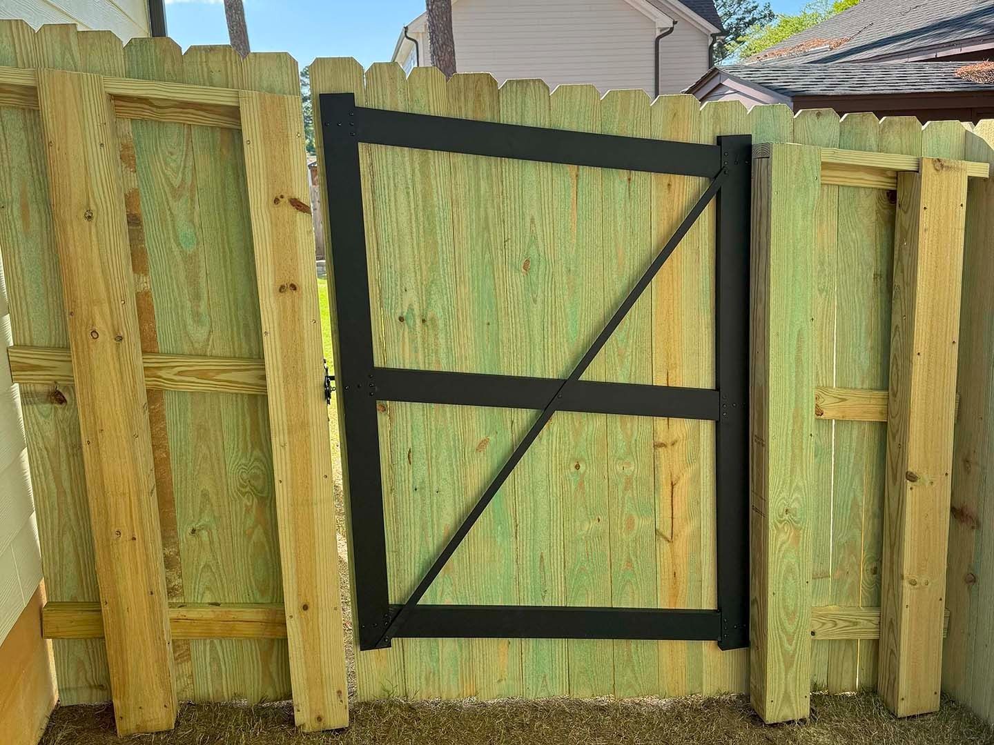 Wooden gate with black metal frame and diagonal brace, set in a wooden fence.