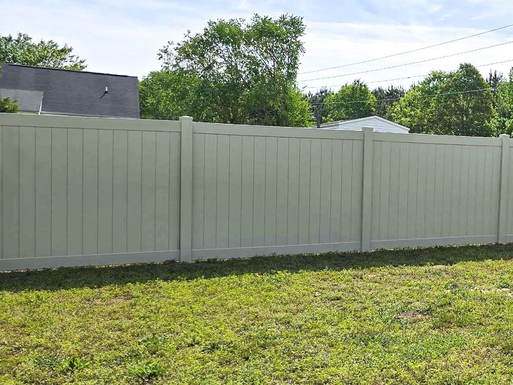 Tan privacy fence in a grassy yard with trees and power lines in the background.