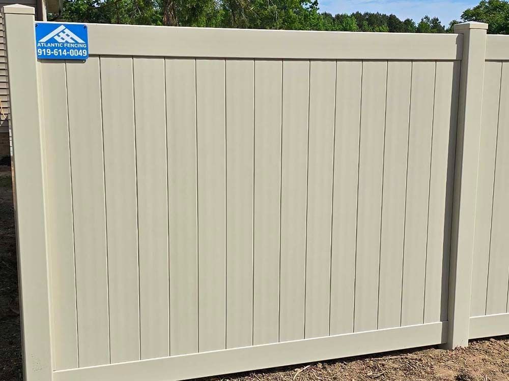 Tan vertical vinyl fence with a company sign.