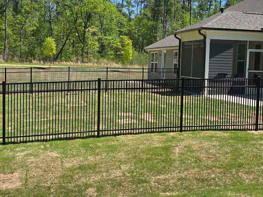 Black metal fence around a grassy yard, separating it from a pond and a house with a screened porch.