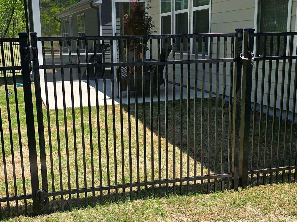 Black metal fence in a yard, with a house and grass in the background.