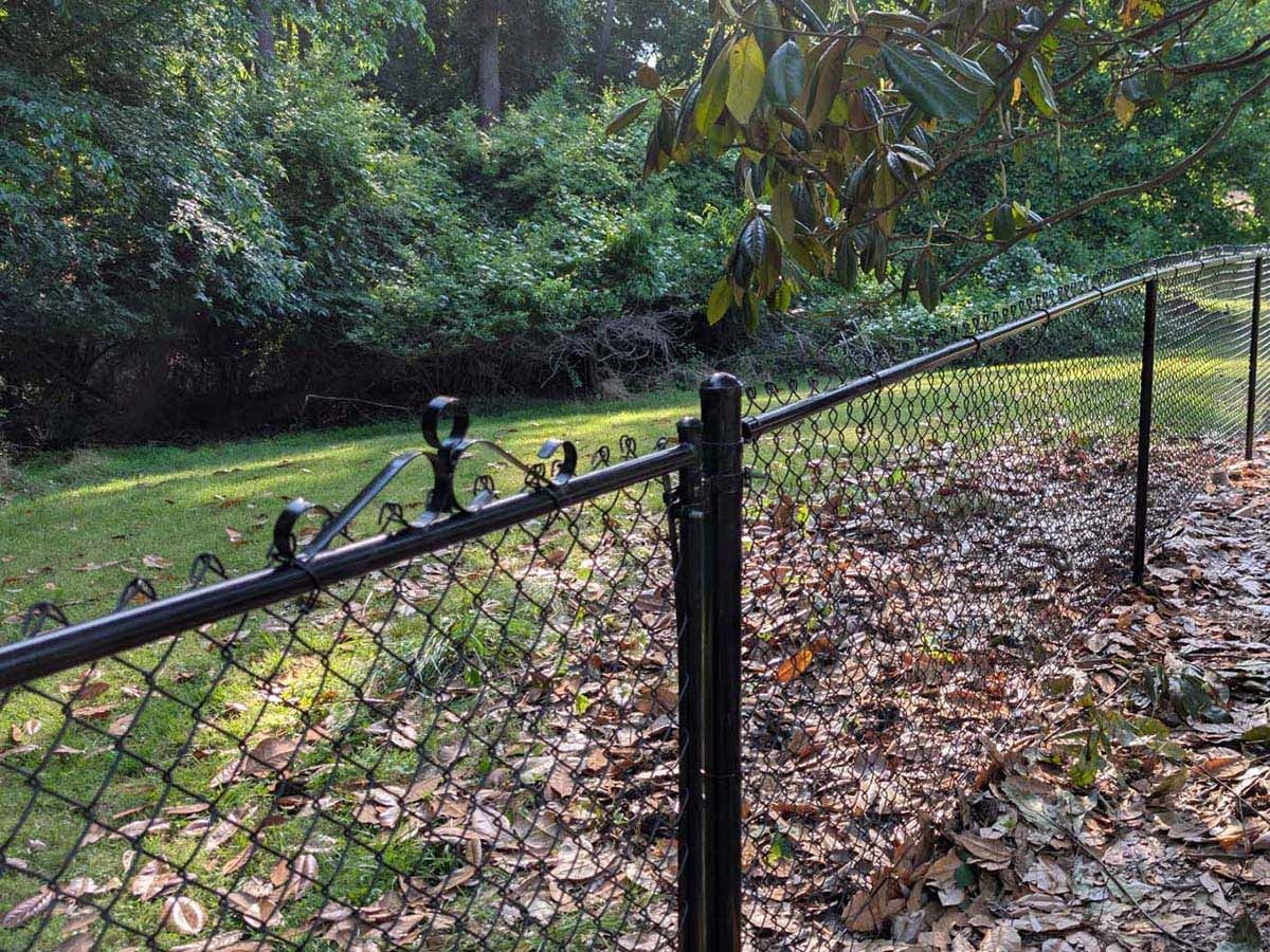 Black chain-link fence in a yard, with a background of trees and leaves.