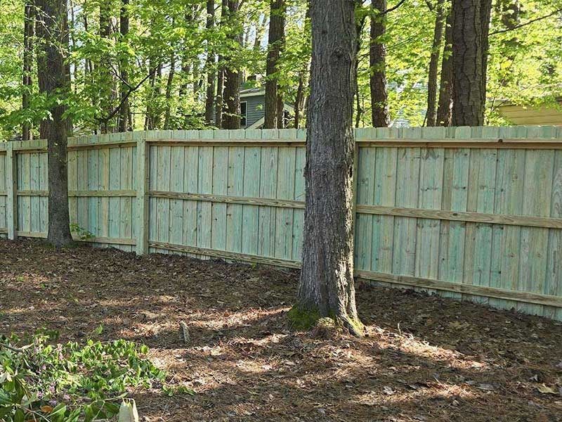 A wooden fence in a wooded area with trees and fallen leaves.